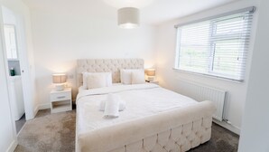 A bedroom with a large bed, bedside lamps, a radiator, and a window with blinds. - Castle View Chalet by Clonlum Cottages (Newry)