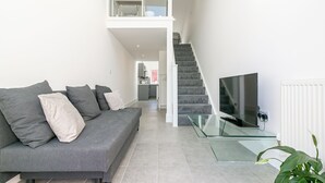 A modern living room with a grey sofa, a glass coffee table, and a staircase leading to an upper level. - King Pin Corner (Stevenage)