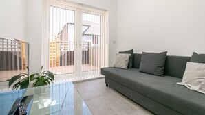 A living room with a grey sofa, a glass coffee table, and a sliding glass door leading to a balcony. - King Pin Corner (Stevenage)