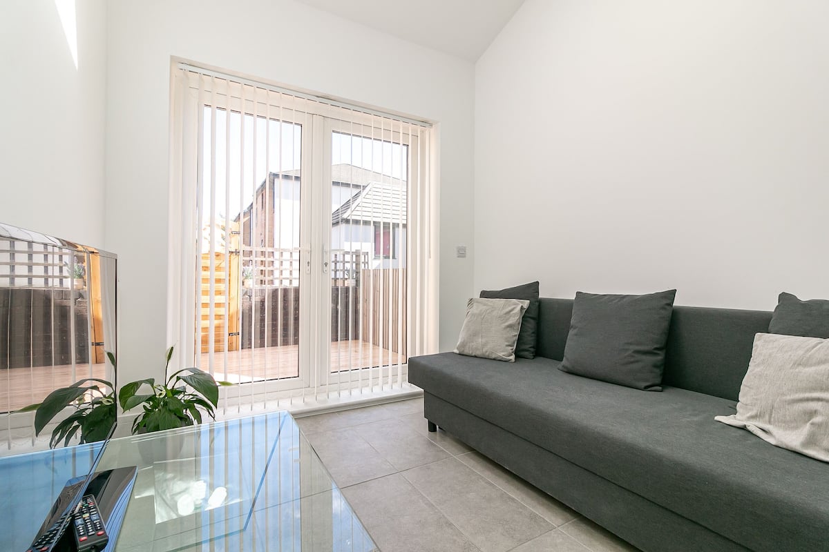 A living room with a grey sofa, a glass coffee table, and a sliding glass door leading to a balcony.