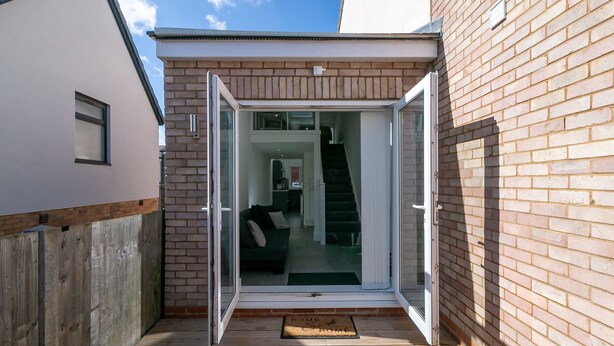A modern house with a wooden deck, a glass door leading to a living area, and a brick exterior wall. - King Pin Corner (Stevenage)