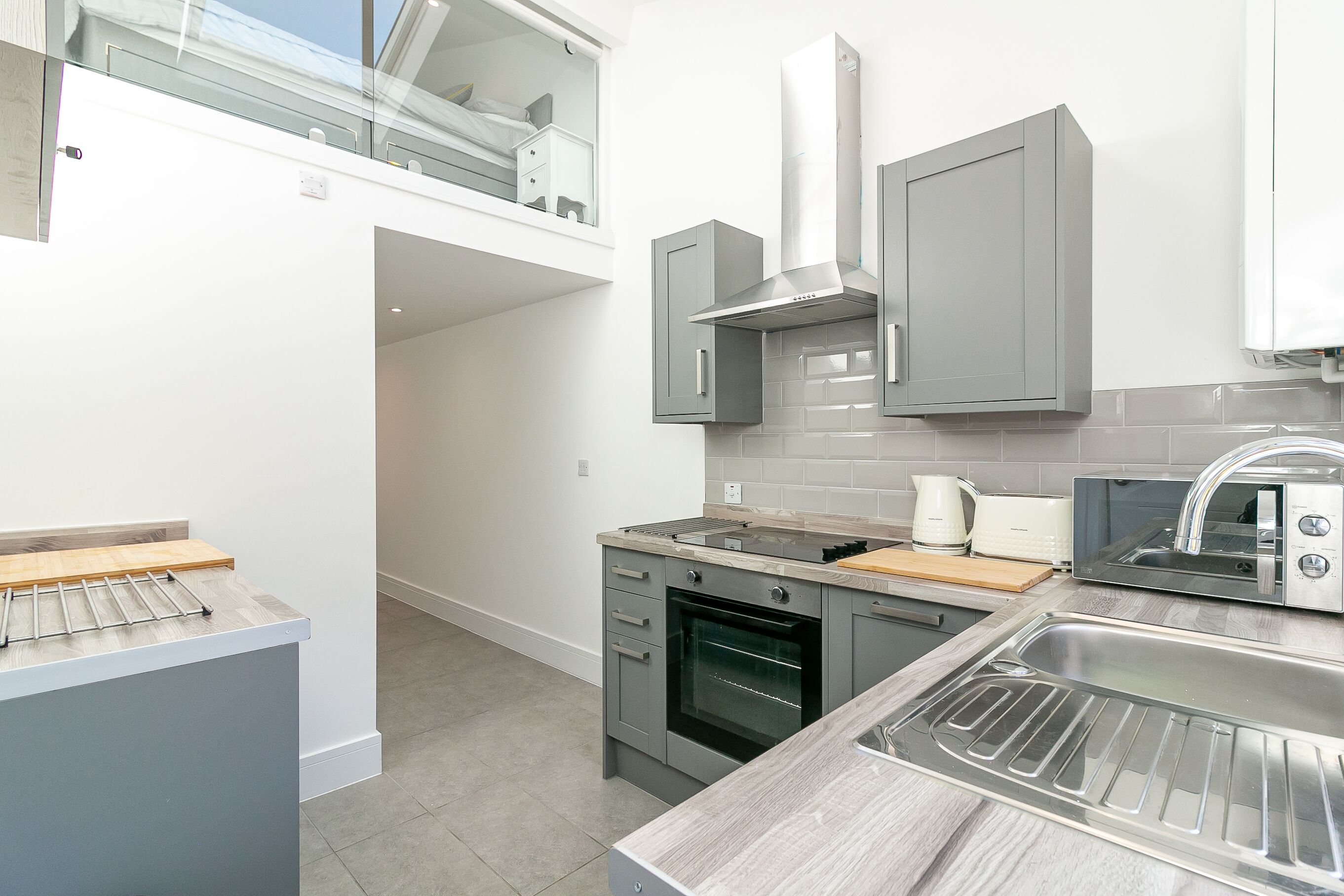 A modern kitchen with grey cabinets, a built-in oven, a microwave, and a stainless steel sink.