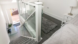 A modern bedroom with a glass staircase, a bedside table with a lamp, and a large bed. - King Pin Corner (Stevenage)