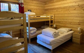 A wooden cabin room with bunk beds, a small bedside table, and a window with curtains.