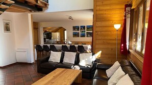 Ett mysigt vardagsrum med ett soffbord i trä, en svart lädersoffa och en matplats med stolar och ett bord.