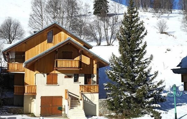 A wooden chalet with a balcony, a staircase, and a snow-covered landscape.