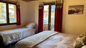 Ett hotellrum med två sängar, röda gardiner, en tavla på väggen och utsikt över en byggnad utanför.