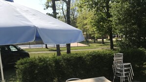 Ein Sitzbereich im Freien mit Tisch und Stühlen, einem überdachten Sonnenschirm und einem in der Nähe geparkten Auto.
