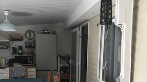 Eine kleine Küche mit Mikrowelle, Kühlschrank und Holzschränken. Ein Esstisch mit Stühlen und ein Fenster mit Jalousien sind ebenfalls vorhanden.