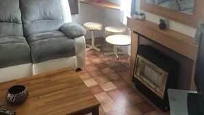 Ein gemütliches Wohnzimmer mit grauem Sofa, Couchtisch aus Holz, einem kleinen runden Tisch, Kamin und einem Spiegel darüber.
