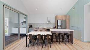 A modern kitchen with a central island, a dining area with chairs, and a view of the adjacent living space.