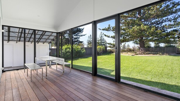 A modern patio with a wooden deck, a metal table, and a glass door leading to a grassy backyard.
