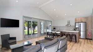 A modern kitchen with a large island, a dining area with a sofa and chairs, and a flat-screen TV mounted on the wall.