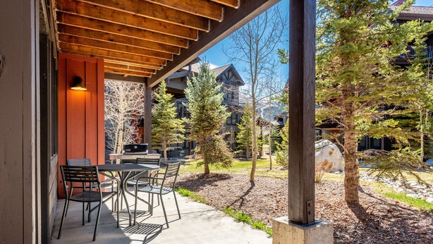Une terrasse extérieure dotée d’une pergola en bois, d’une table avec des chaises, et offrant une vue sur une montagne et des bâtiments en arrière-plan.