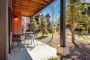 An outdoor patio with a wooden pergola, a table with chairs, and a view of a mountain and buildings in the background.