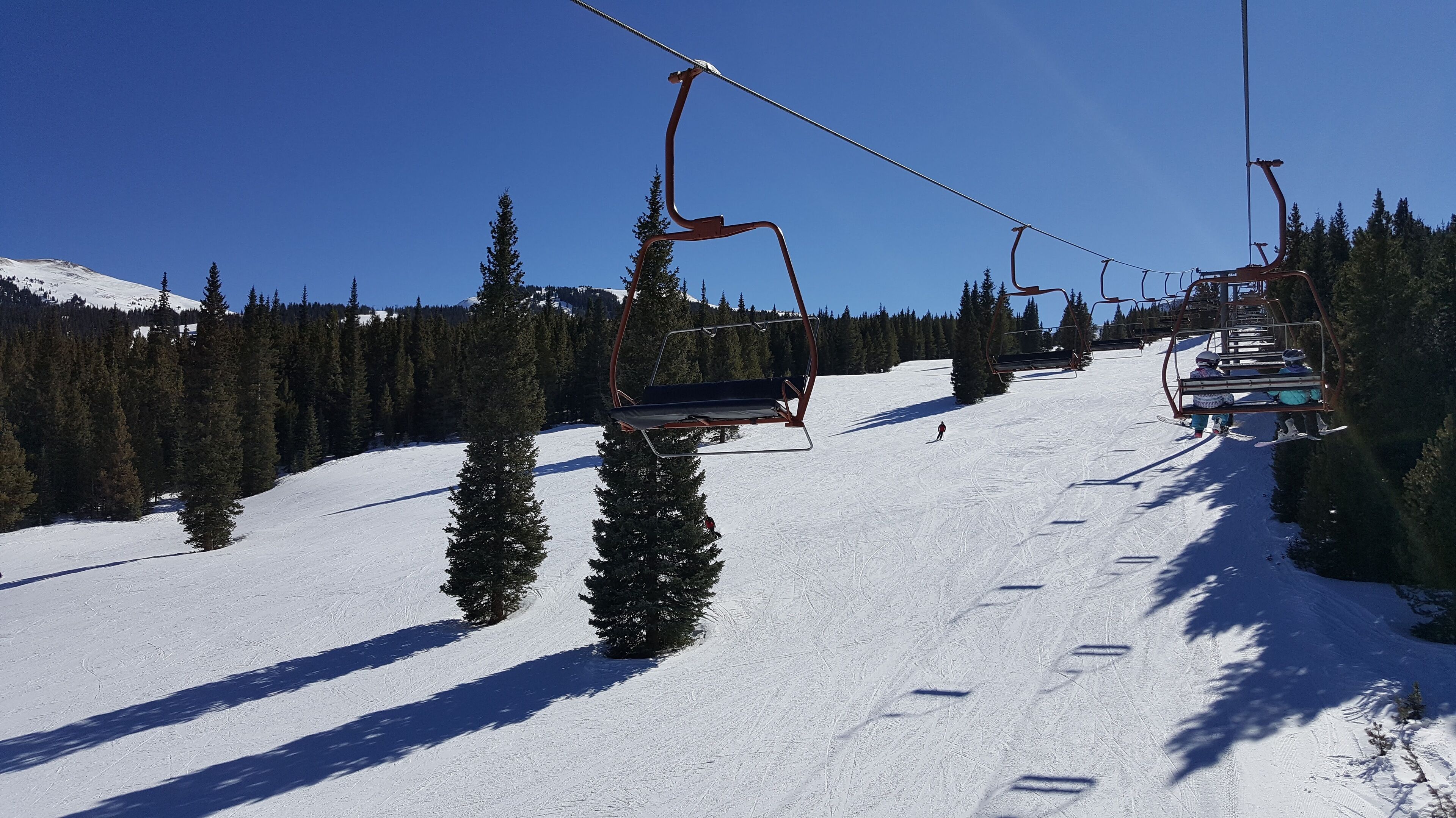 En skilift med stole hængende på kabler, omgivet af sneklædte skråninger og snebærende træer.