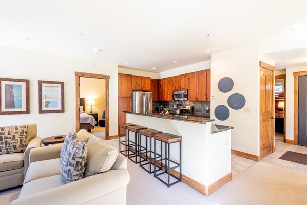 A modern kitchen with wooden cabinets, a stainless steel refrigerator, and a bar area with stools. - West Village Two Bedroom Townhome, walk to the beginner slopes! Free WiFi (Copper Mountain)