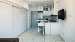 Una cocina compacta con armarios blancos, un refrigerador integrado, una pequeña isla y un televisor de pantalla plana montado en la pared.