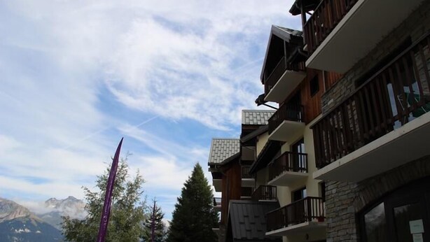 A multi-story building with balconies, a stone facade, and a view of mountains.