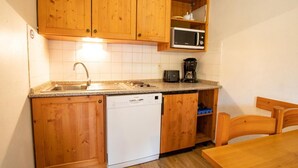 A compact kitchen with wooden cabinets, a microwave, a coffee maker, and a dishwasher.