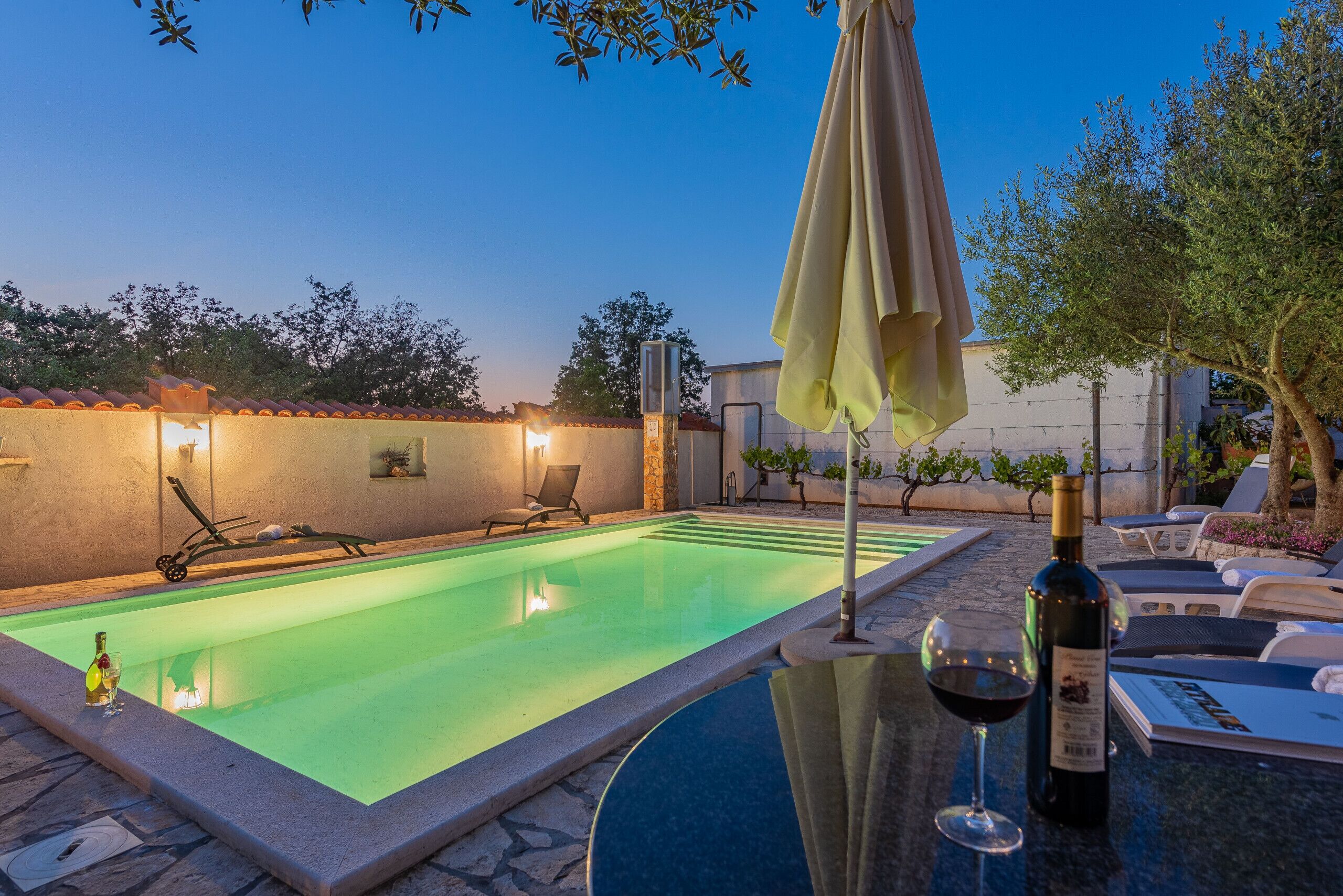 Ein Swimmingpool mit Liegestühlen und Sonnenschirmen, eine Weinflasche und ein Glas auf einem Tisch.