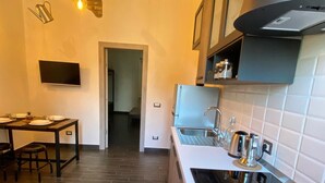 Une cuisine moderne avec un plancher en bois foncé, une cuisinière encastrée et un évier. On y trouve également un coin repas avec une table et des chaises, ainsi qu’un téléviseur fixé au mur.