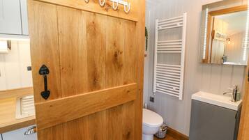 A wooden door with a towel rack, a white toilet, a sink, and a mirror with lights.