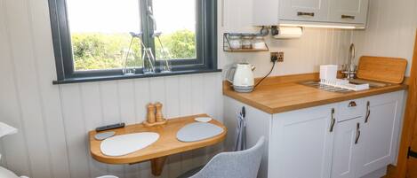 A compact kitchen with a wooden countertop, two grey chairs, a window with a view, and white cabinets.