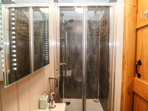 A bathroom with a glass-enclosed shower, a vanity with a mirror, and a wooden door. - Cwt Y Rhos (Holyhead)