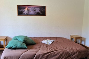 Een kamer met een bed, twee houten nachtkastjes, een groen kussen, een bruine dekbedovertrek en een ingelijst schilderij aan de muur.