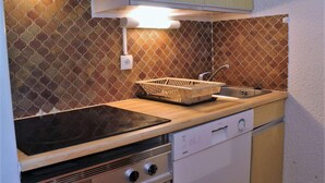 A compact kitchen with a stove, dishwasher, and a sink with a basket. - 50m from resort center, 2nd floor, swimming pool, balcony, tv, ski locker, 32m², Risoul (Risoul)