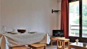 A dining area with a table set for two, a television on a wooden stand, and a window with curtains. - 50m from resort center, 2nd floor, swimming pool, balcony, tv, ski locker, 32m², Risoul (Risoul)