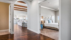 A spacious hallway with wooden flooring leading to a bedroom with a bed and a nightstand.