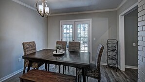 A dining room with a dark wooden table, wicker chairs, a chandelier, and a window with a view. - Three Bedroom Home Reservoir Getaway (Brandon)