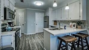 A modern kitchen with white cabinetry, stainless steel appliances, and a central island with bar stools. - Three Bedroom Home Reservoir Getaway (Brandon)