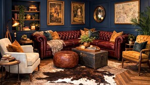 Um quarto em azul escuro com um sofá de couro, um banquinho redondo, uma mala antiga e um globo na parede.