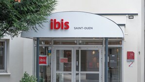 De buitenkant van het ibis Saint-Ouen hotel, met een duidelijke ingang, borden en een bloempot.
