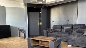 Een moderne woonkamer met een grijze hoekbank, een houten salontafel en een zwarte stoel.