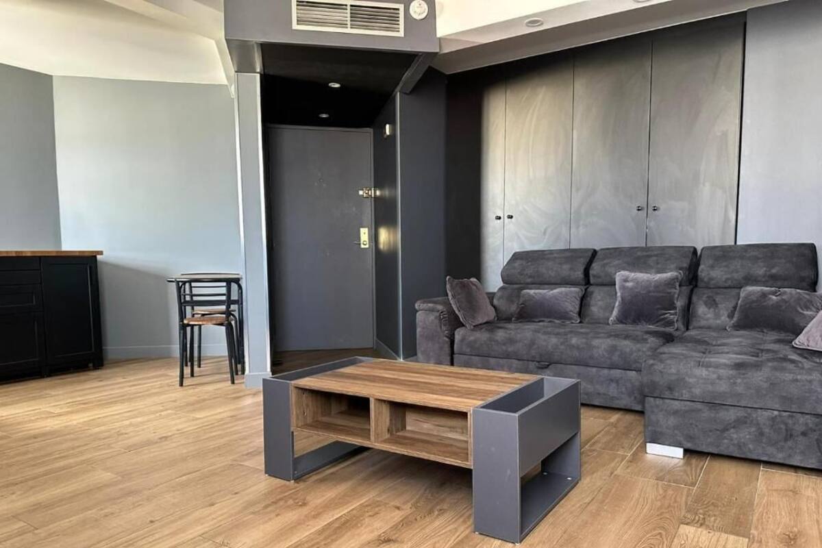Un salon moderne avec un canapé d’angle gris, une table basse en bois et un fauteuil noir.