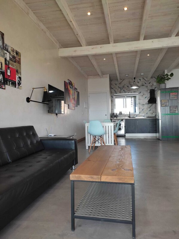A spacious living area with a black leather sofa, a wooden coffee table, and a kitchen in the background. - Apartamentos Torre Vigia (Torrox)