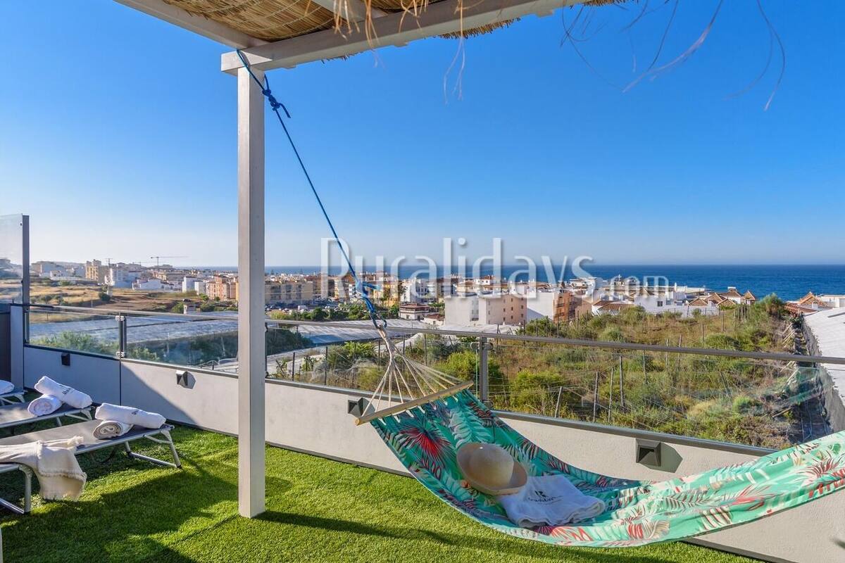 A balcony with a hammock, lounge chairs, and a view of the sea and cityscape.