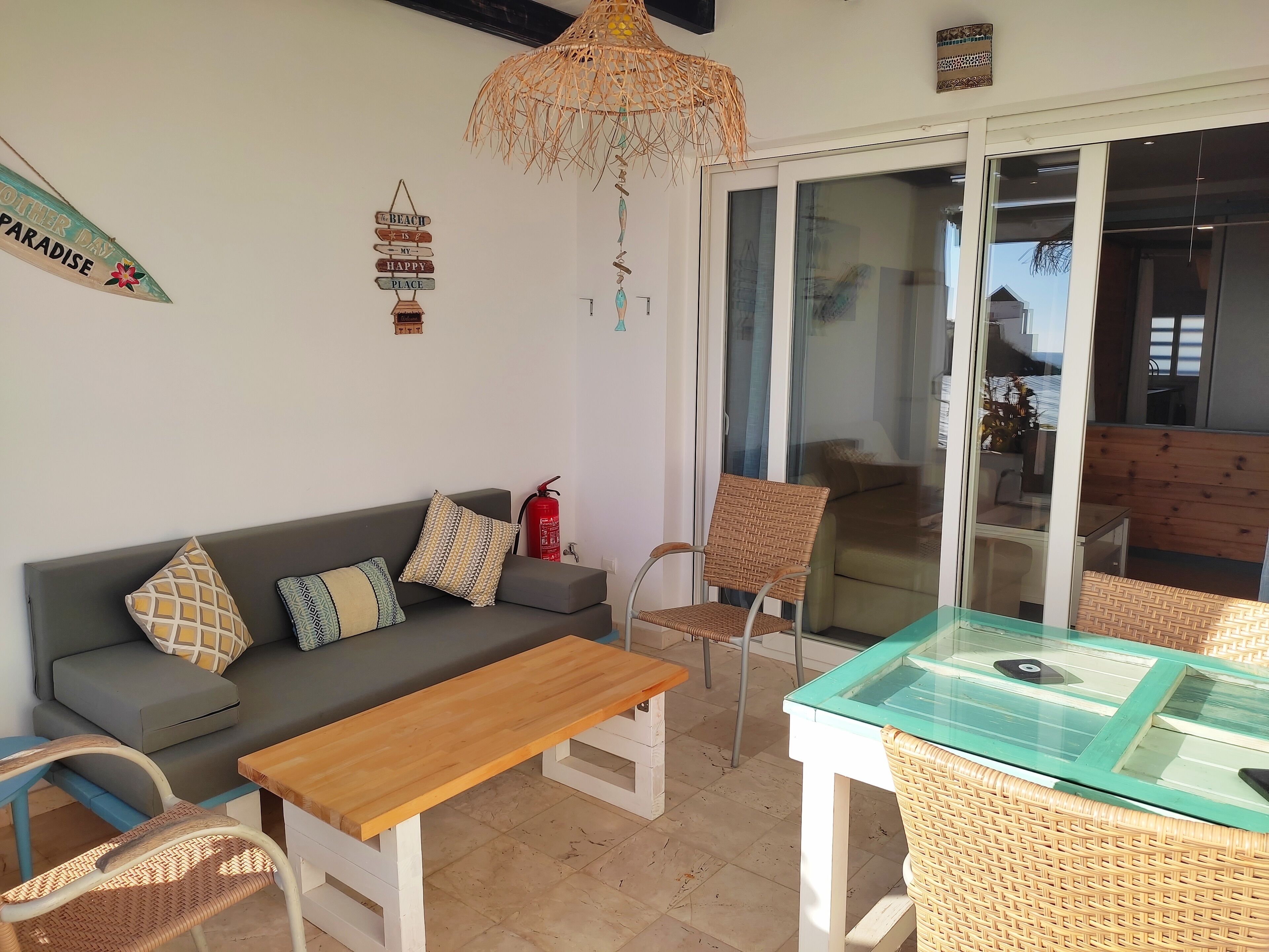 A cozy living area with a sofa, a wooden table, wicker chairs, and a glass-top table.