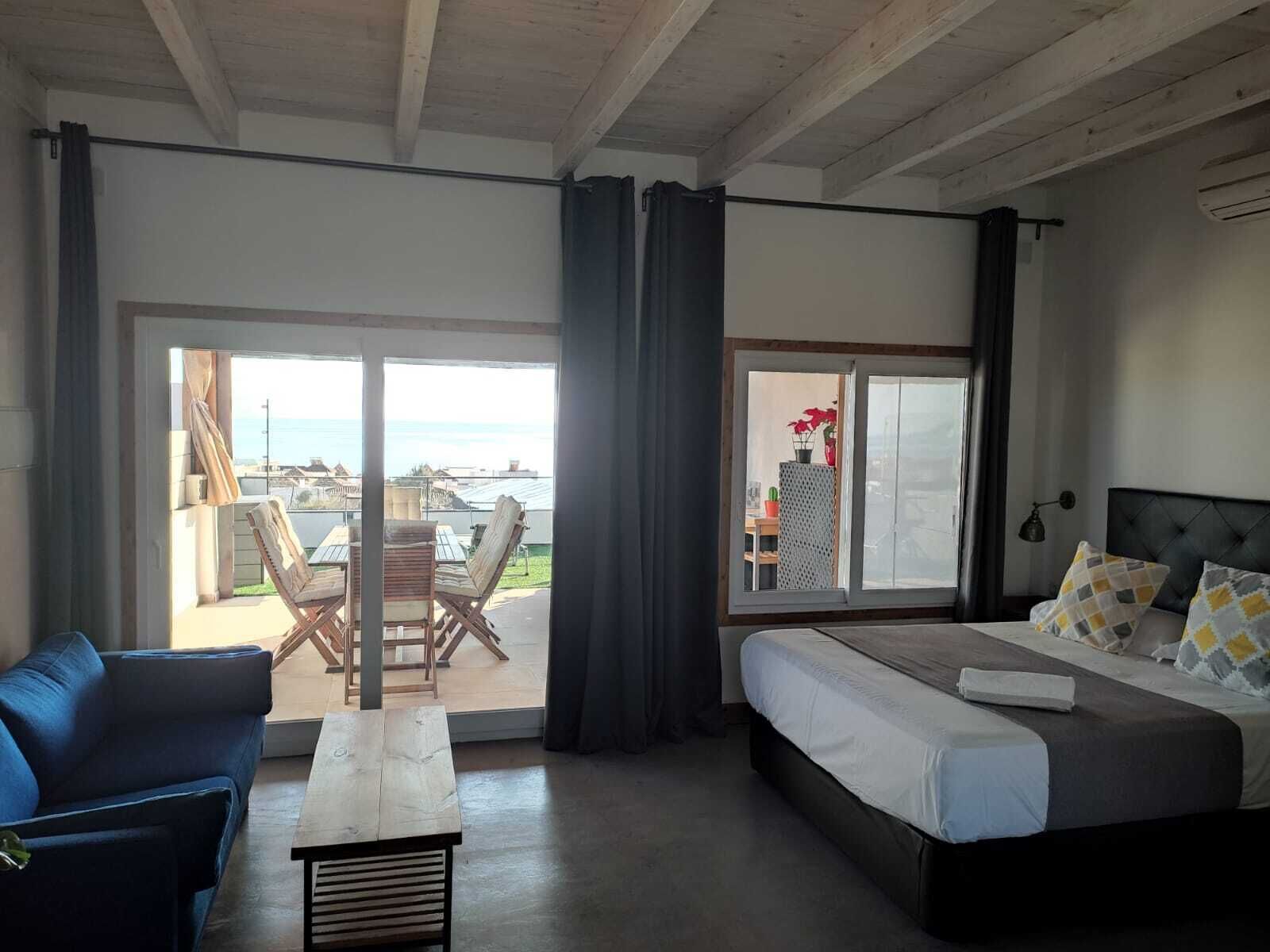 Een slaapkamer met een bed, een bank, een tafel en een balkon met stoelen.