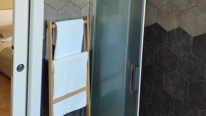 Un baño moderno con paredes de azulejos hexagonales, cabina de ducha de vidrio y toallero de madera.