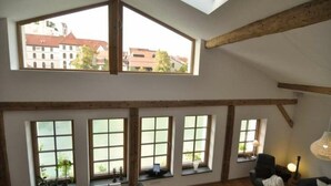 Een kamer met hoge plafonds, grote ramen en zichtbare houten balken.