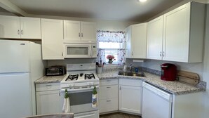 A compact kitchen with white cabinets, a microwave, a stove, a sink, and a red coffee maker.