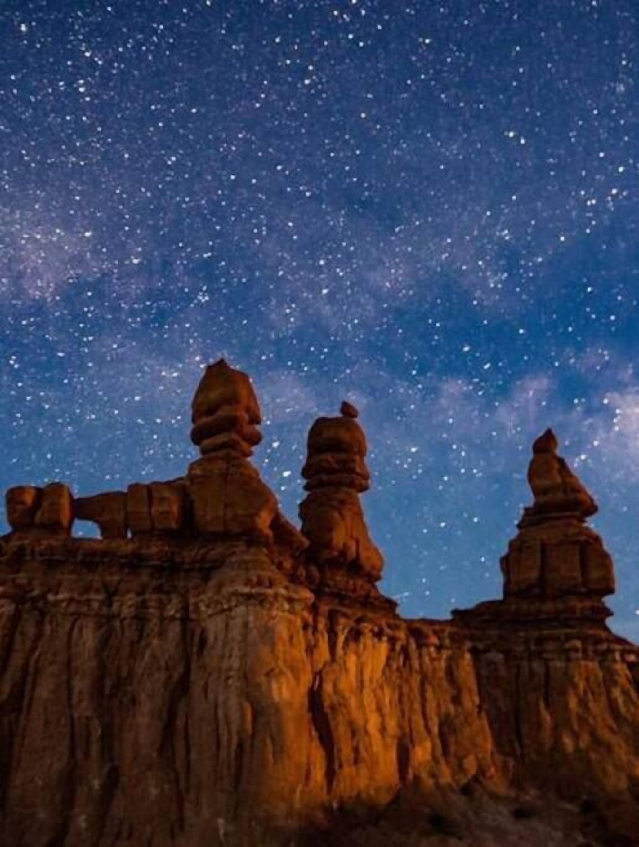 A starry night sky over a rocky landscape with balanced rock formations.