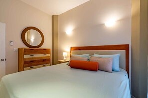 Une chambre à coucher avec un lit, une commode en bois, un miroir rond et des lampes fixées au mur.