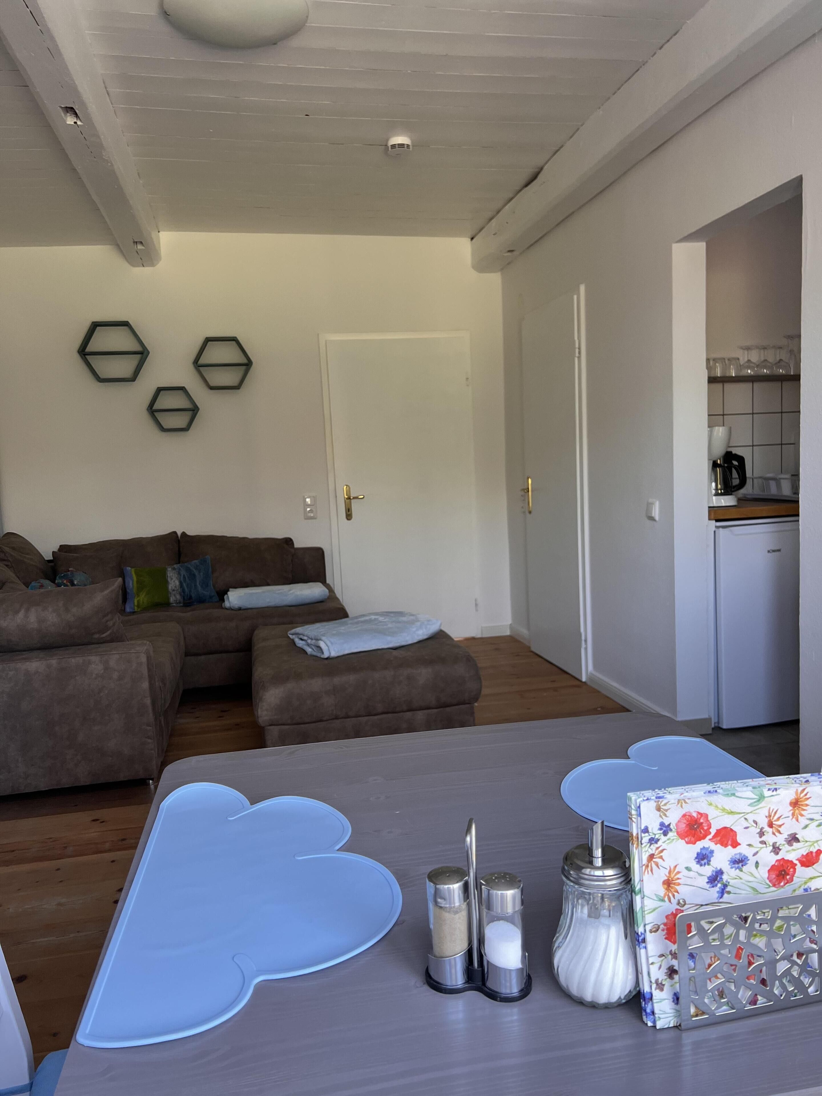 A modern living room with a sectional sofa, a coffee table with a geometric design, and a kitchen area visible through an open door.