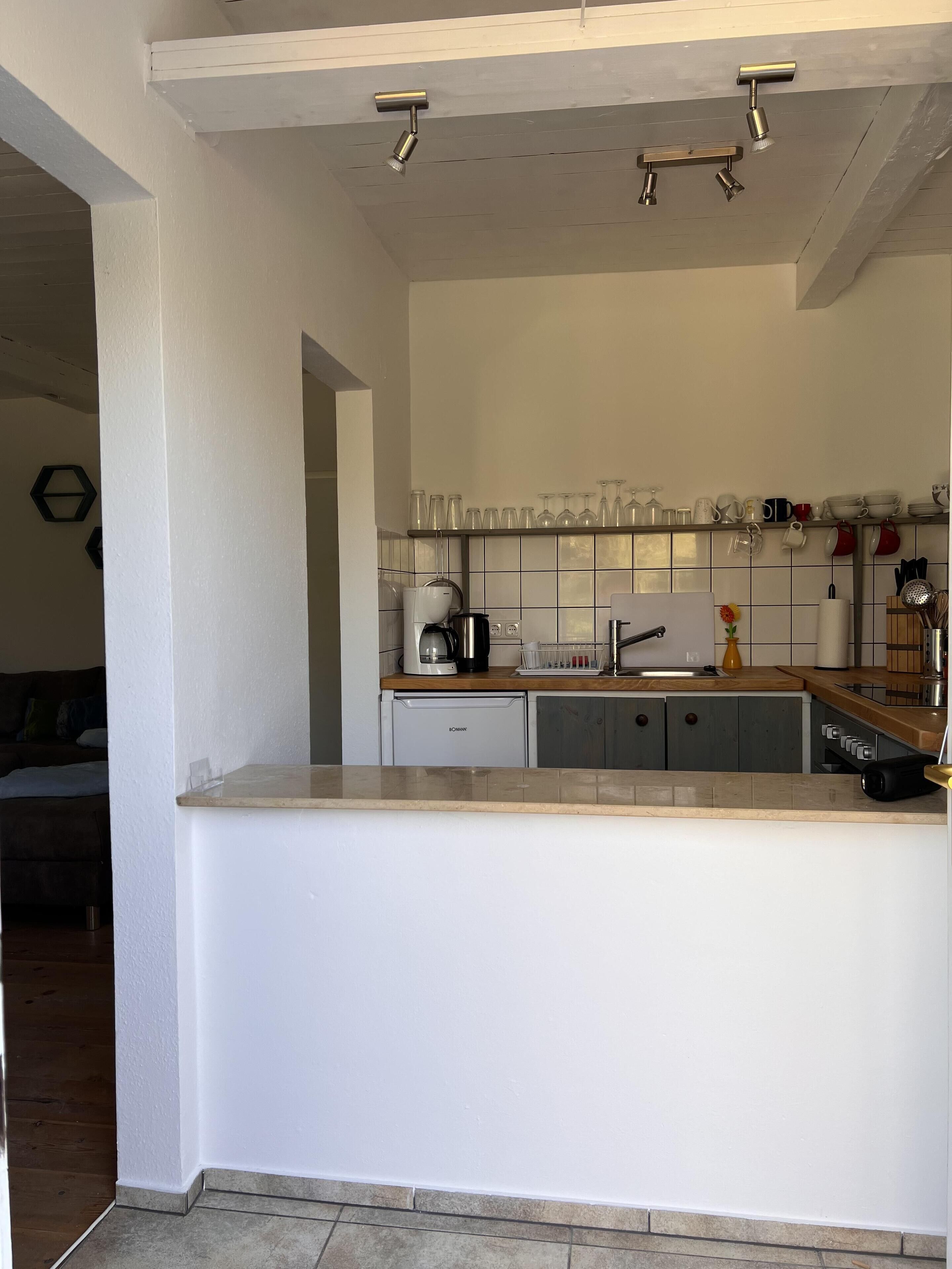 A modern kitchen with a central island, white cabinetry, a coffee machine, and a variety of kitchen utensils.